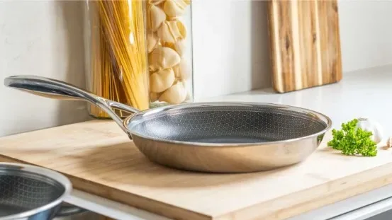A Matero stainless steel frying pan on a wooden board beside garlic and fresh pasta