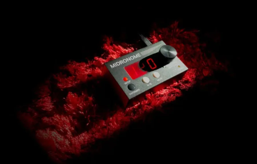 The Midronome, a compact grey hardware master clock, on black inside a burst of red powder